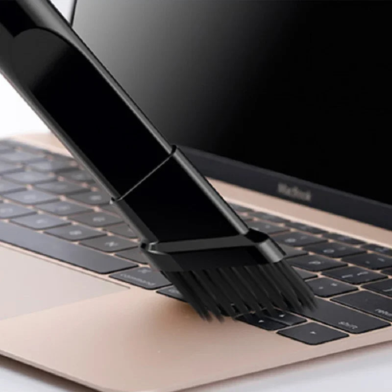 Black nylon cleaning brush sweeping dust from a gold laptop keyboard.