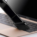 Black nylon cleaning brush sweeping dust from a gold laptop keyboard.
