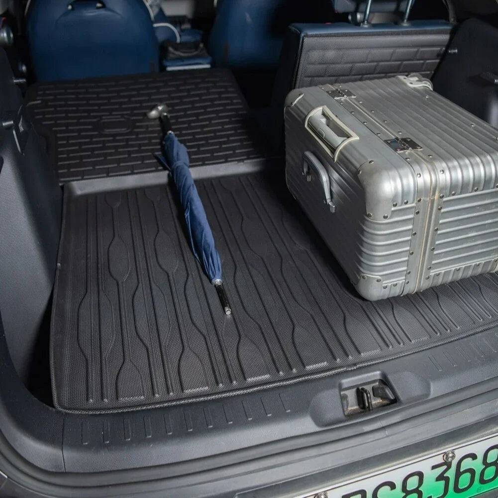Black textured TPE trunk mat protecting the car boot with a silver suitcase and blue umbrella.