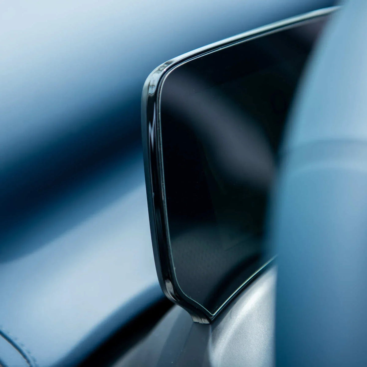 Close-up of a sleek black touchscreen infotainment display integrated into a blue leather car interior.