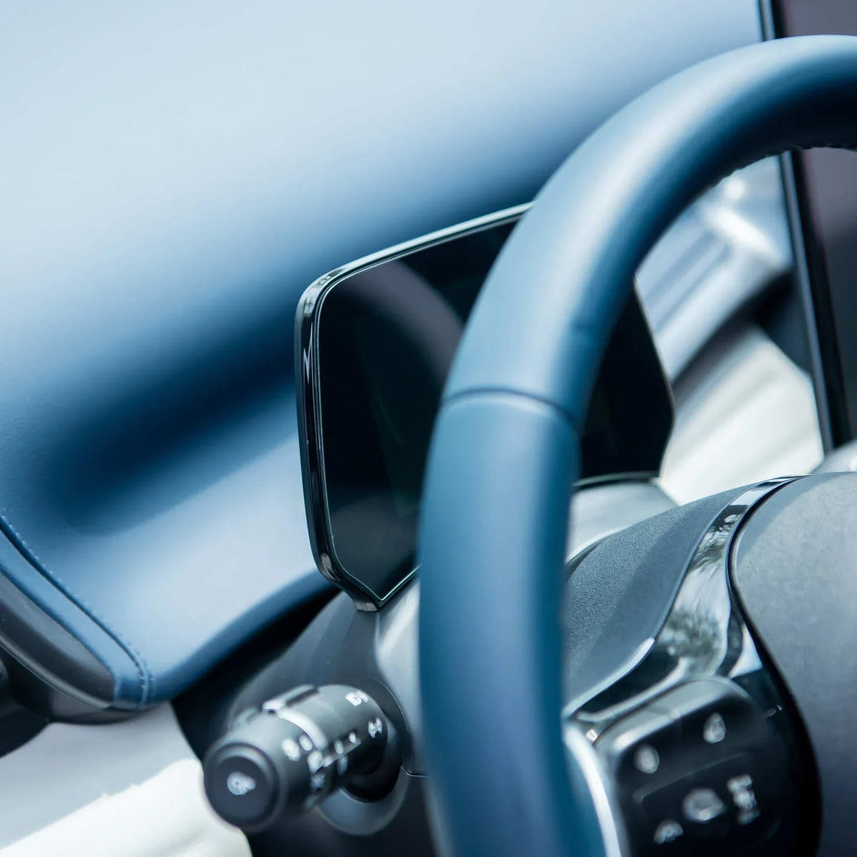 Blue leather-wrapped steering wheel and sleek black digital dashboard display in a car interior.