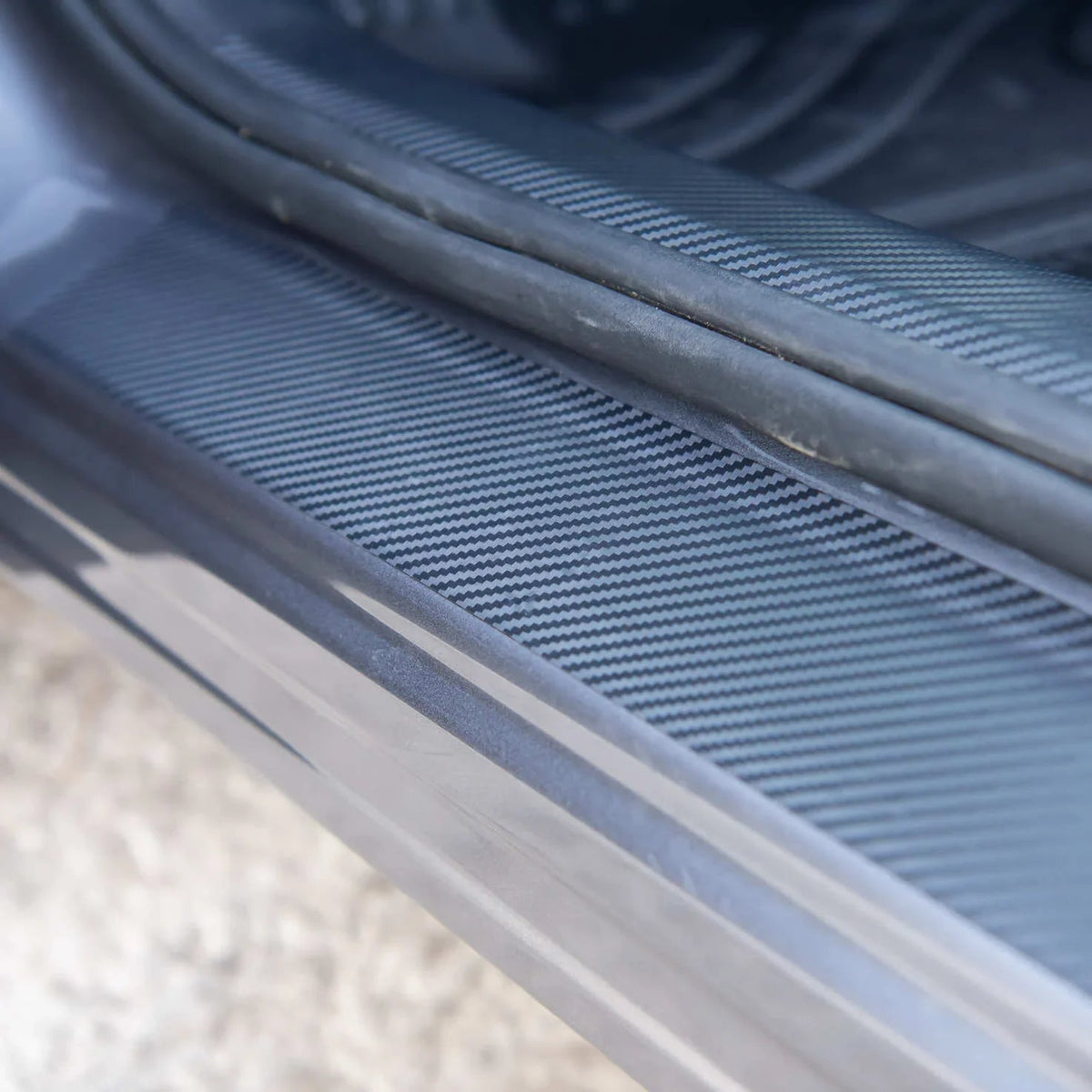 Close-up of a grey carbon fiber texture car door sill protector.