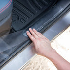 Hand installing a grey carbon fiber texture door sill protector on a car