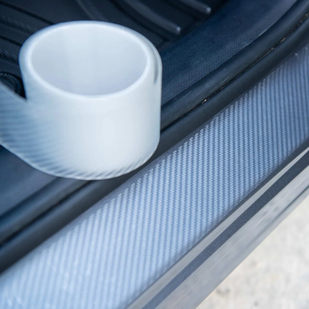 Close-up of a grey carbon fiber car door sill protector with a white cup.