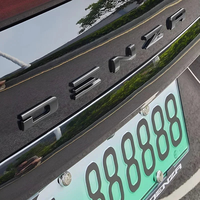 Glossy black Denza chrome emblem badge mounted on a sleek dark car trunk.