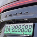 Black Denza license plate frame with a sleek metallic finish and embossed logo.