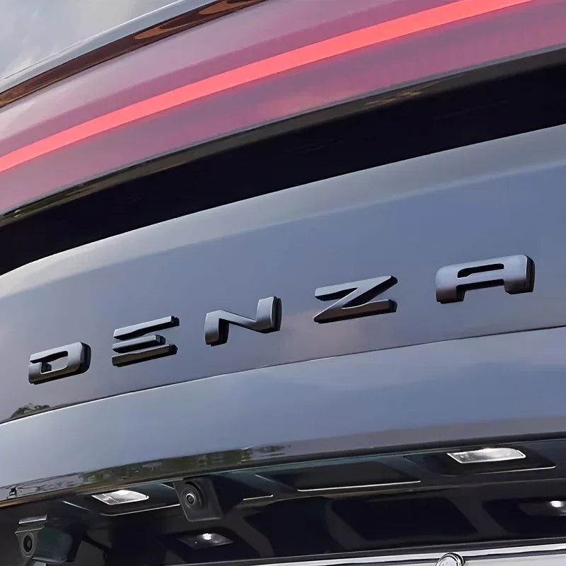 Close-up of black DENZA emblem on a sleek, dark metallic car rear bumper with red light strip.