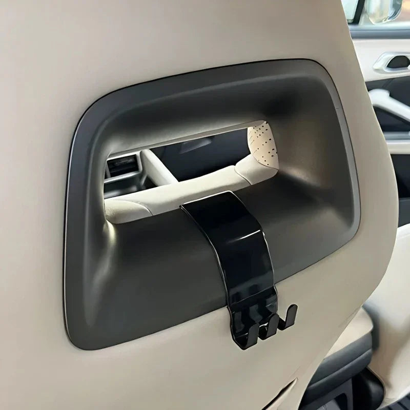 Black durable plastic car seat back hook installed in a beige interior for convenient storage.