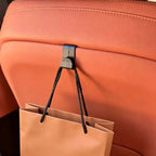 Black durable plastic car seat headrest hook holding a tan shopping bag on tan leather interior.