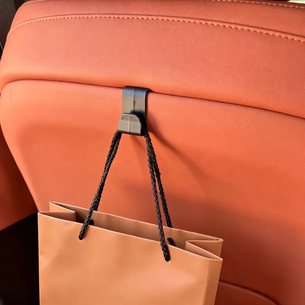Black durable plastic car seat headrest hook holding a tan shopping bag on tan leather interior.