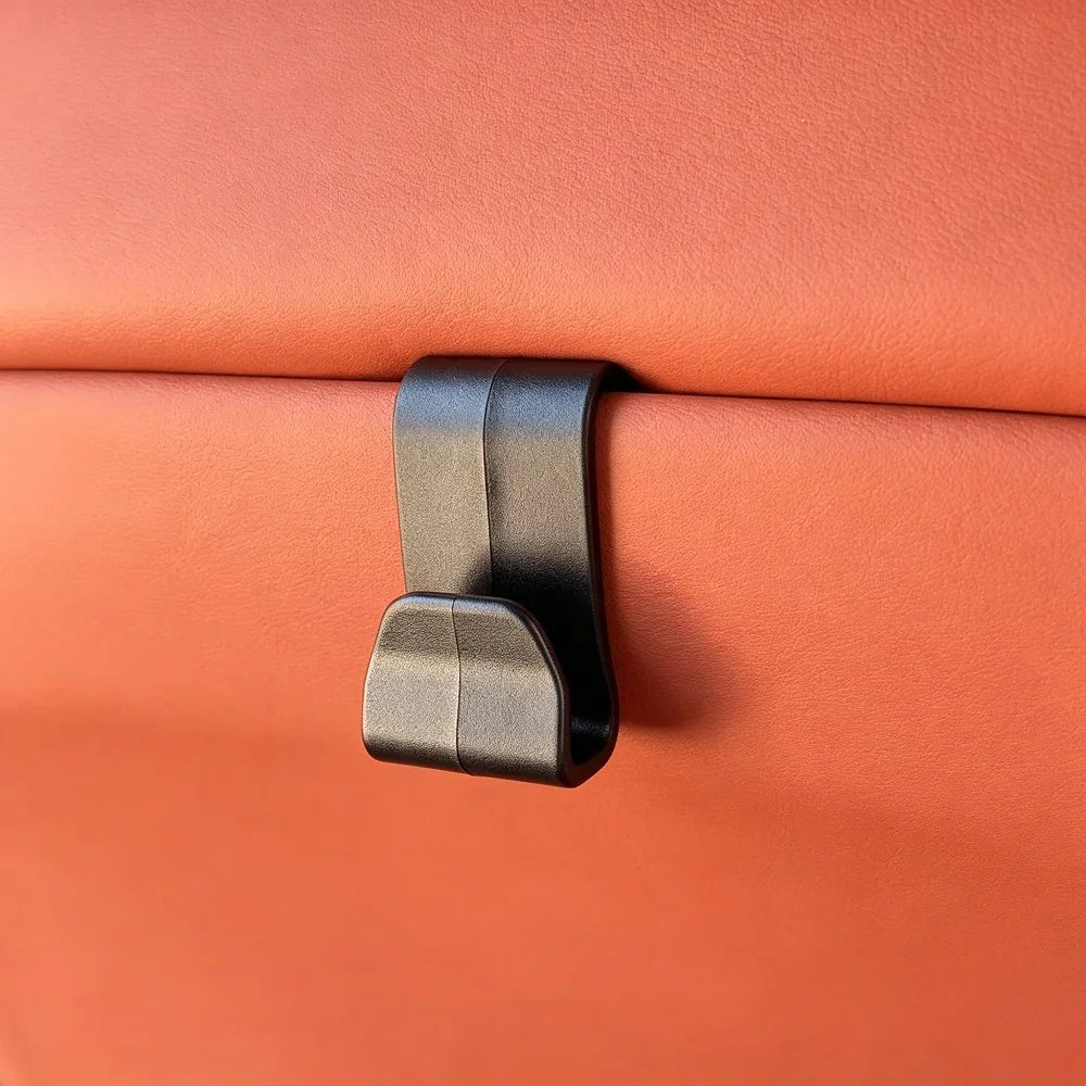 Black matte plastic car seat hook mounted on premium brown leather upholstery.