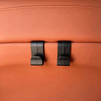 Two black matte plastic seat hooks mounted on premium tan leather car upholstery.