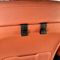 Black durable plastic seat back hooks mounted on premium tan leather car upholstery.
