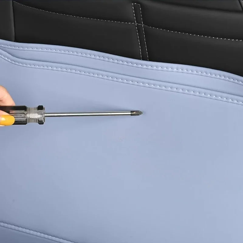 Close-up of a screwdriver testing the durability of light blue synthetic leather car seat covers.