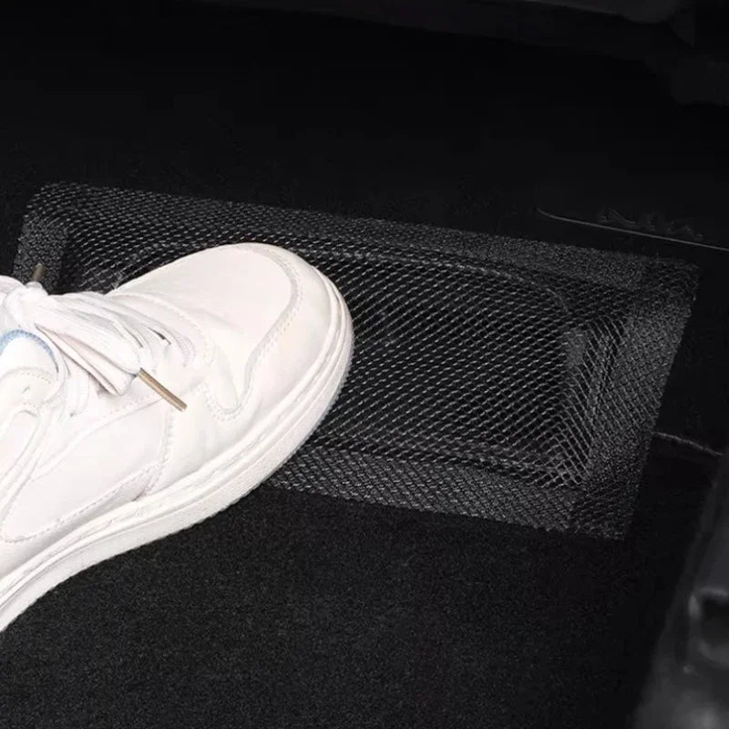 Black mesh storage net organizer installed on the vehicle floor for secure item storage.