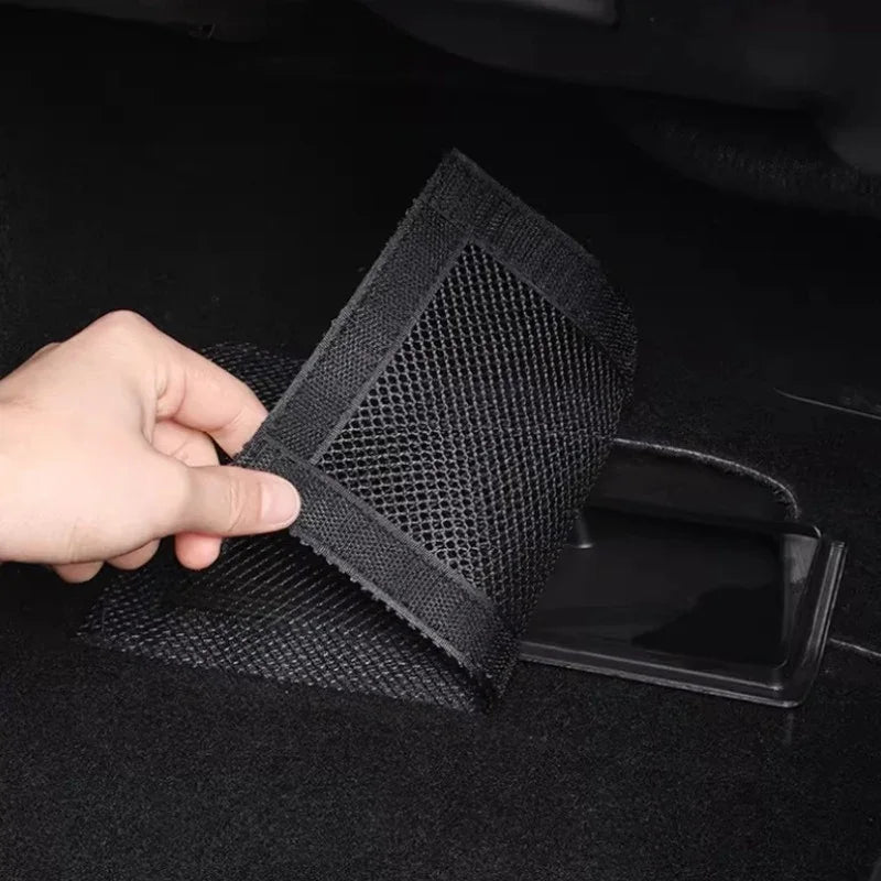 Black mesh storage pocket organizer being installed on a car trunk floor.