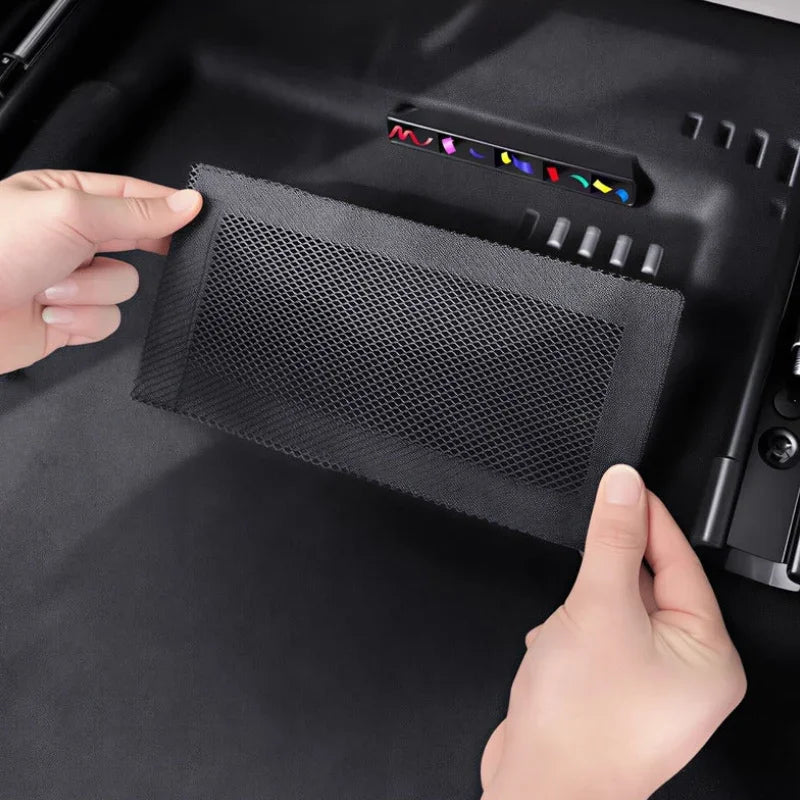 Black mesh storage organizer pocket being installed into a car trunk compartment.