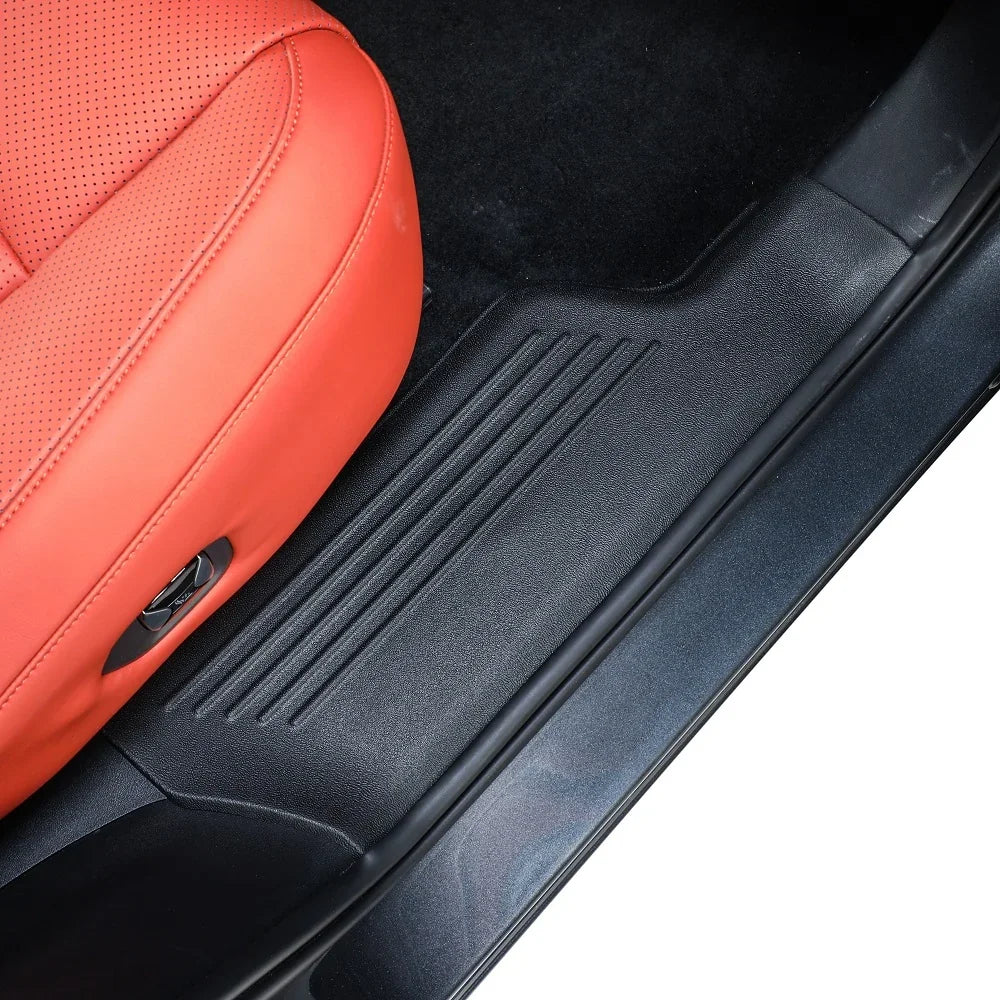 Black textured protective door sill plate installed on a vehicle interior with red leather seats.