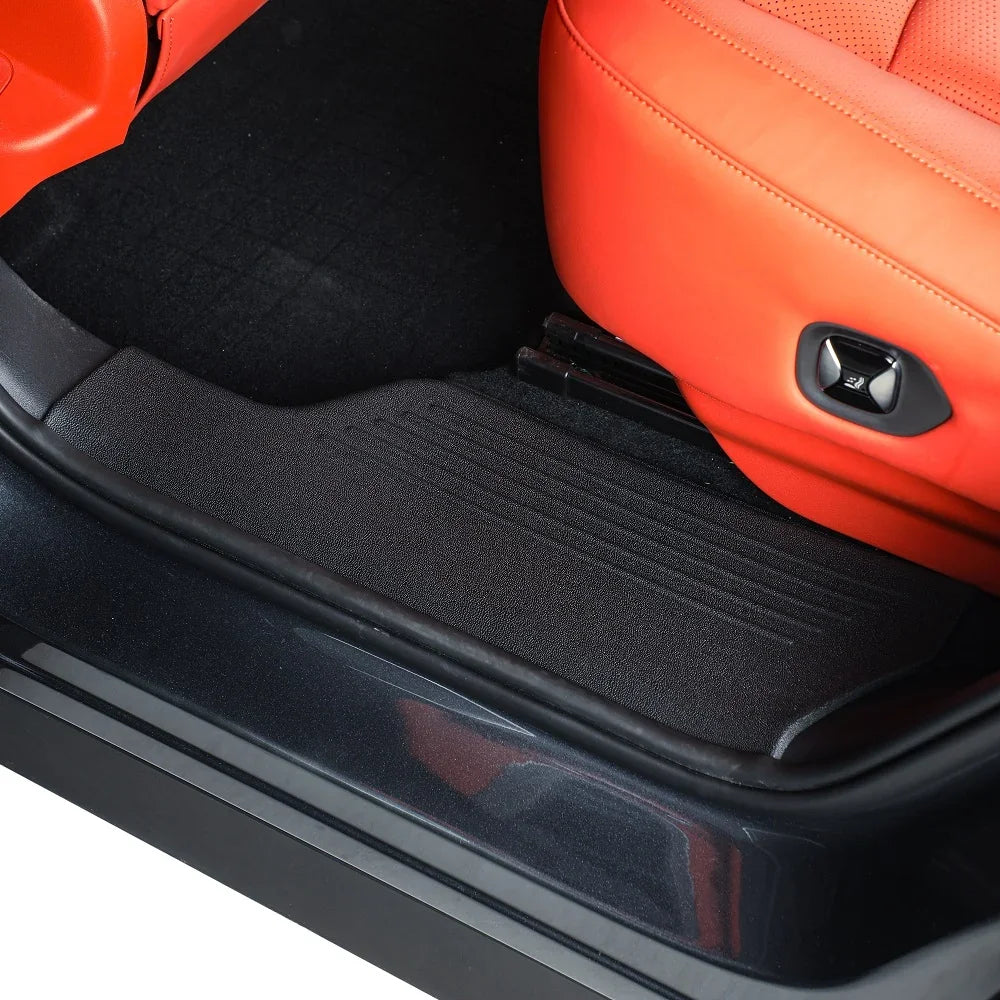 Black heavy-duty rubber door sill protector installed in a car with orange leather seats.