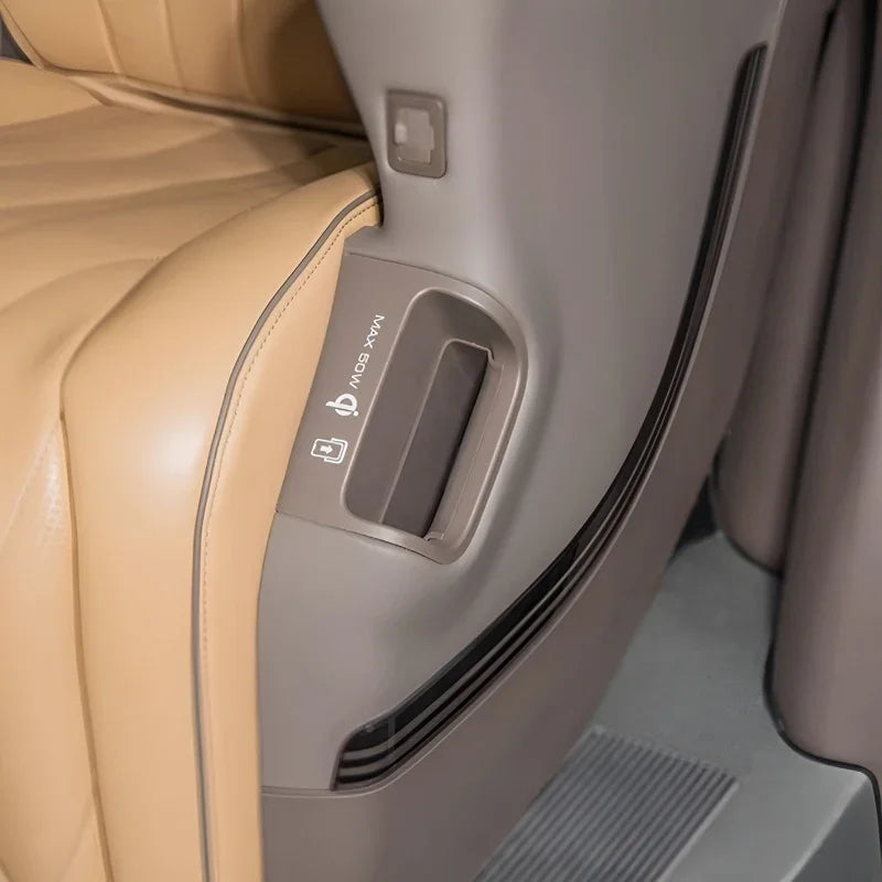 Close-up of a tan leather car seat back with a grey plastic storage pocket and charging port.