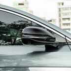 Glossy black aerodynamic side mirror cover with integrated LED indicator for a grey car.