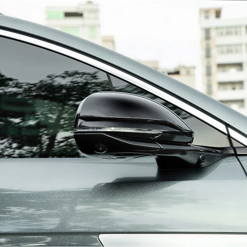 Glossy black aerodynamic side mirror cover with integrated LED indicator for a grey car.