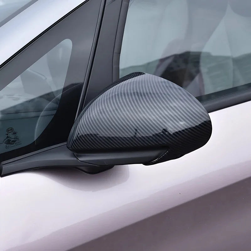Close-up of a car side mirror cover featuring a sleek grey carbon fiber texture.