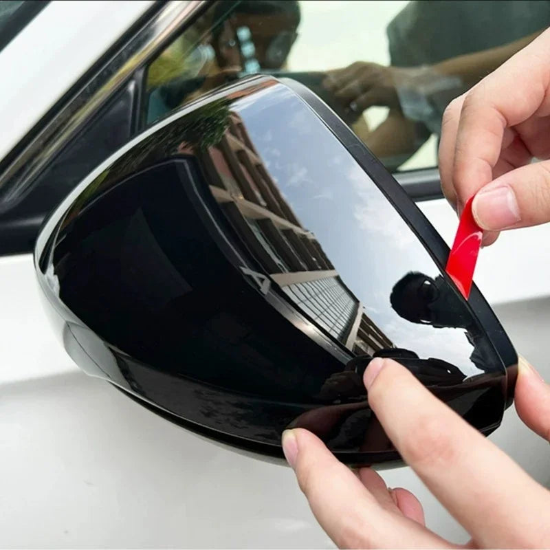 Glossy black protective film being applied to a car side mirror housing.
