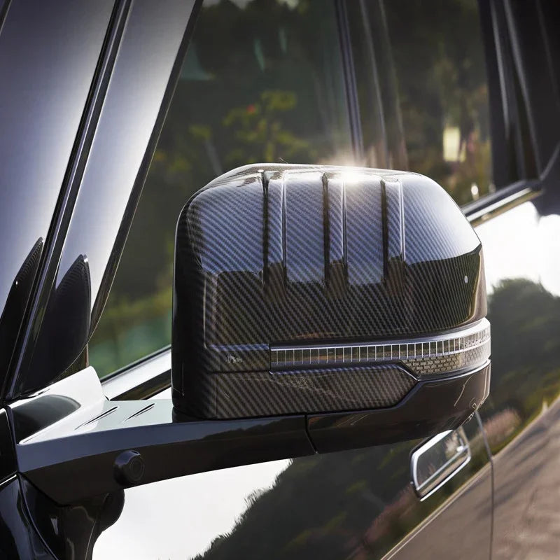 Close-up of a car side mirror cover featuring a grey carbon fiber texture and integrated LED light strip.