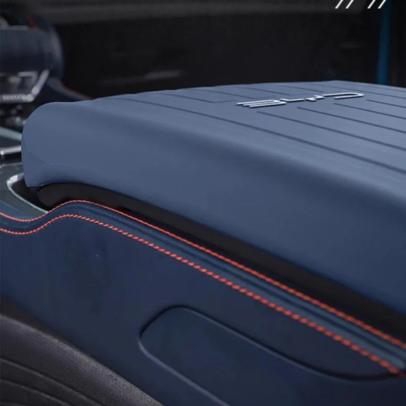 Close-up of a navy blue leather car armrest with orange contrast stitching.