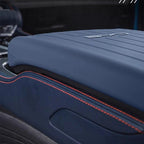 Close-up of a navy blue leather car armrest with orange contrast stitching.