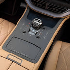 Detailed view of a luxury car center console with tan leather and black matte finishes.
