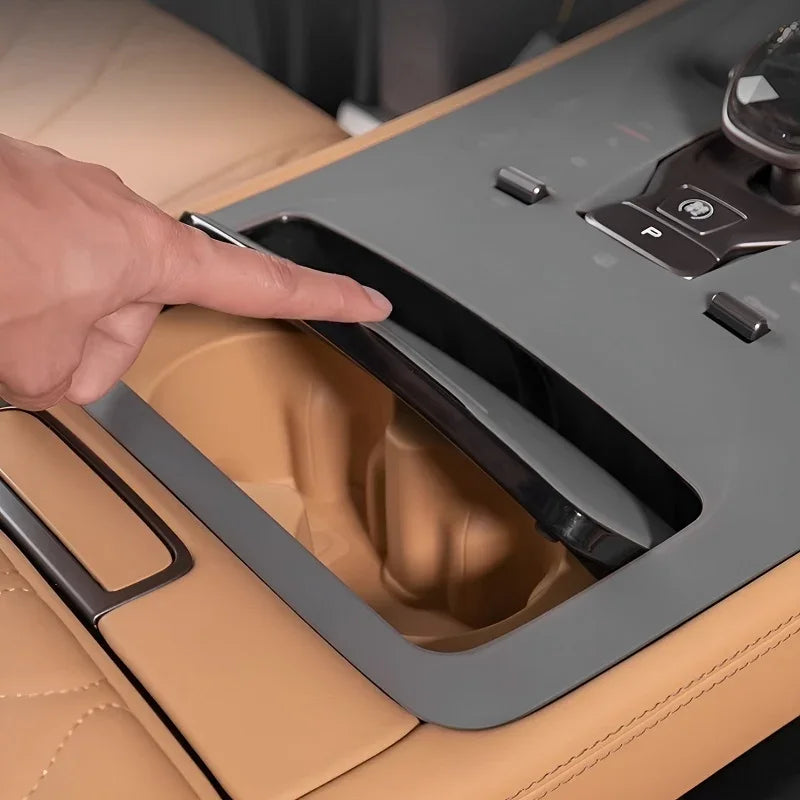 Finger pointing to a sleek black sliding cover on a tan leather car center console compartment.
