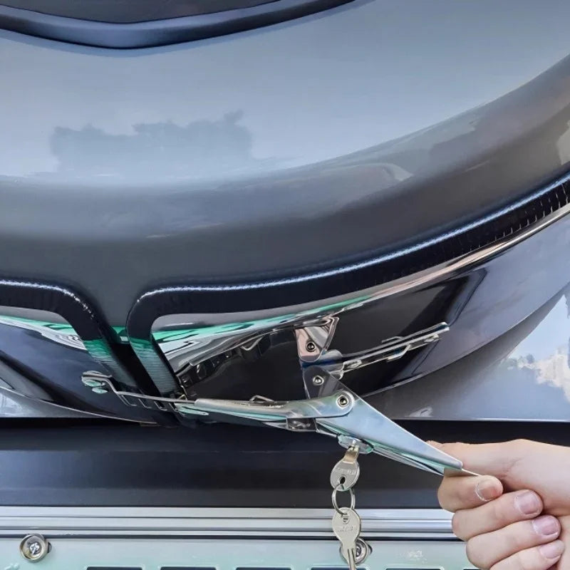 Silver metal spring clamp securing a black protective trim on a grey car bumper.