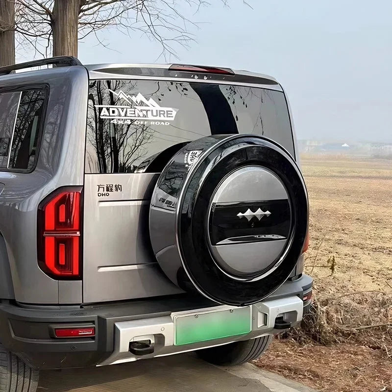 Black and silver hard-shell spare tire cover with mountain graphic on a grey SUV.