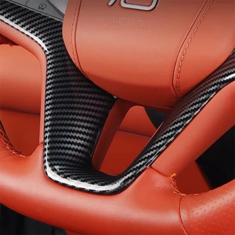 Close-up of a BYD steering wheel featuring orange leather and carbon fiber trim.