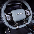 Light blue leather steering wheel with black carbon fiber trim and metallic emblem.