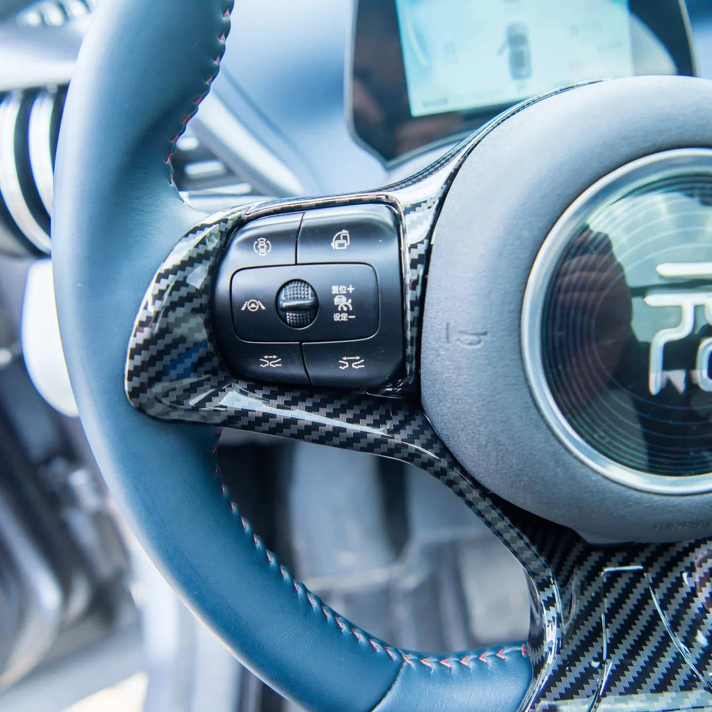 Carbon fiber and blue leather steering wheel with integrated control buttons for BYD vehicles.