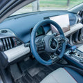 Blue leather steering wheel with carbon fiber accents in a modern car interior.