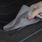 Grey microfiber cloth wiping water off a black textured waterproof car trunk mat.