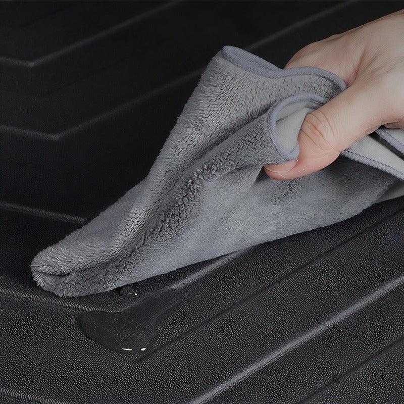 Grey microfiber cloth wiping water off a black textured waterproof car trunk mat.