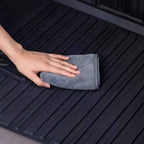 Hand wiping a black textured TPE car floor mat with a grey microfiber cloth.