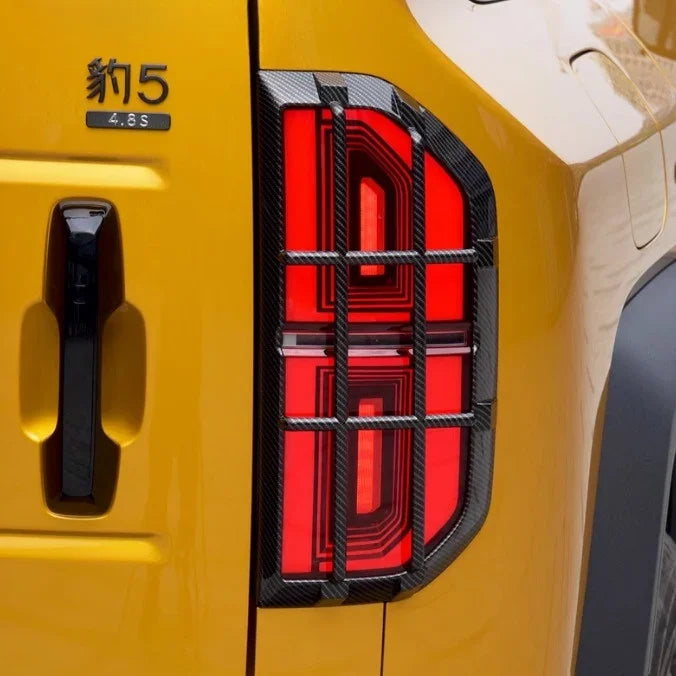 Carbon fiber texture black trim surrounding bright red LED taillight on a yellow car.