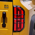 Rugged black protective grille covering a red LED taillight on a yellow vehicle.