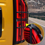 Black matte protective tail light guard installed on a yellow vehicle for durable impact protection.