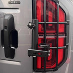 Matte black metal tail light guard with protective grille for a silver vehicle.
