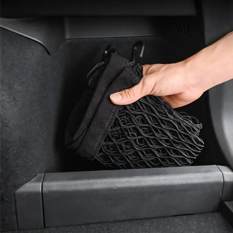 Hand installing a black mesh storage net organizer in a car interior compartment.