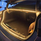 Illuminated car trunk with warm yellow LED strip lighting and black interior lining.