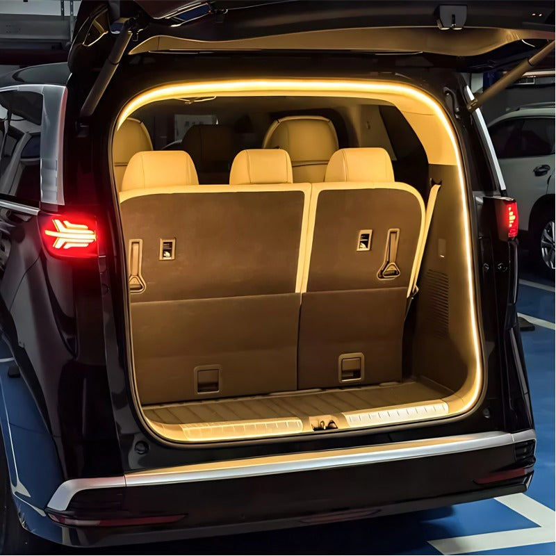 Warm LED light strip illuminating the brown interior of a car trunk with beige leather seats.