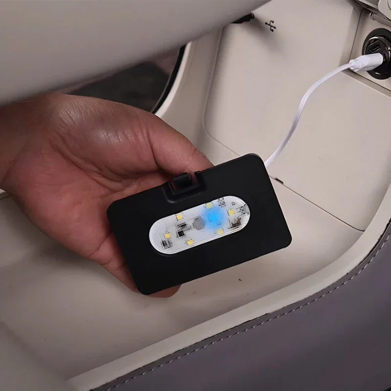 Hand holding a black rectangular LED car interior light plugged into a USB port.